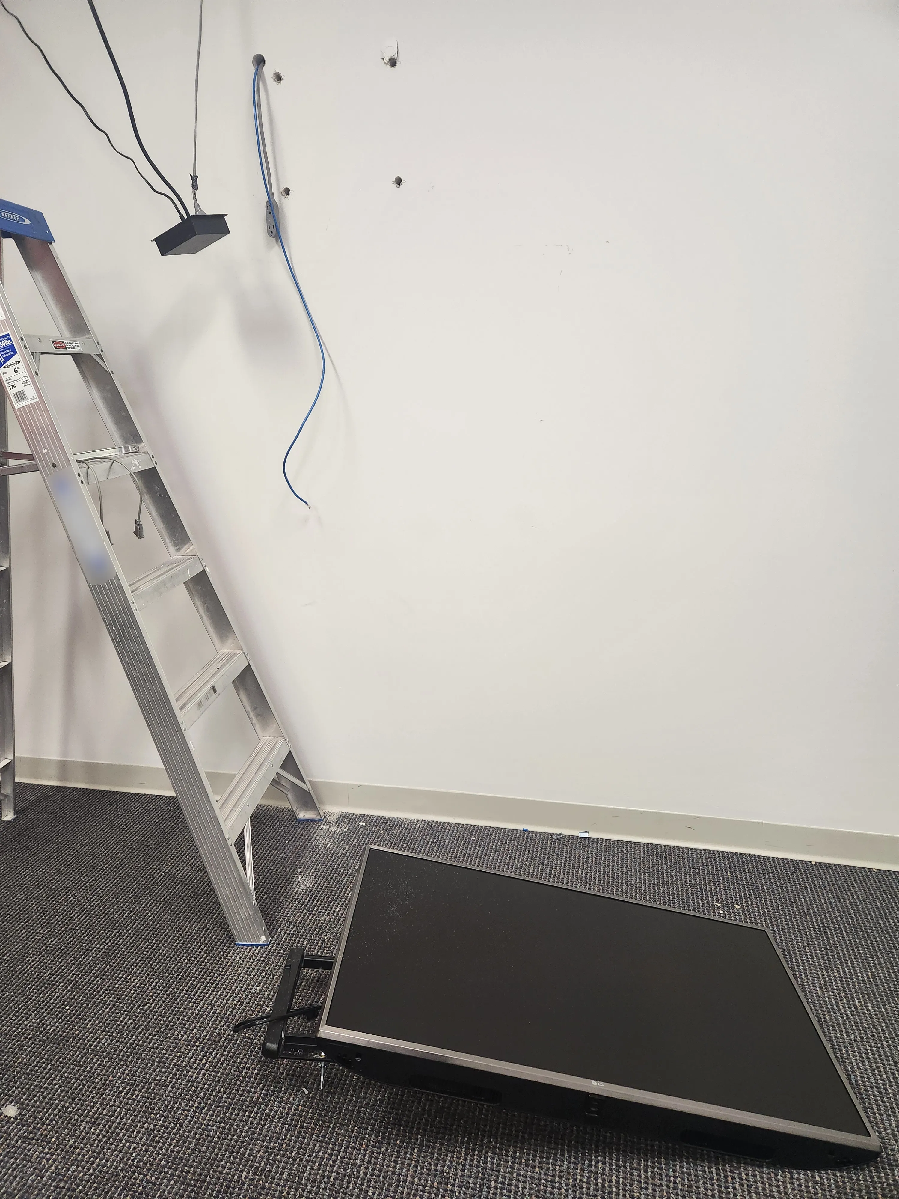 A flatscreen TV on the ground next to a ladder