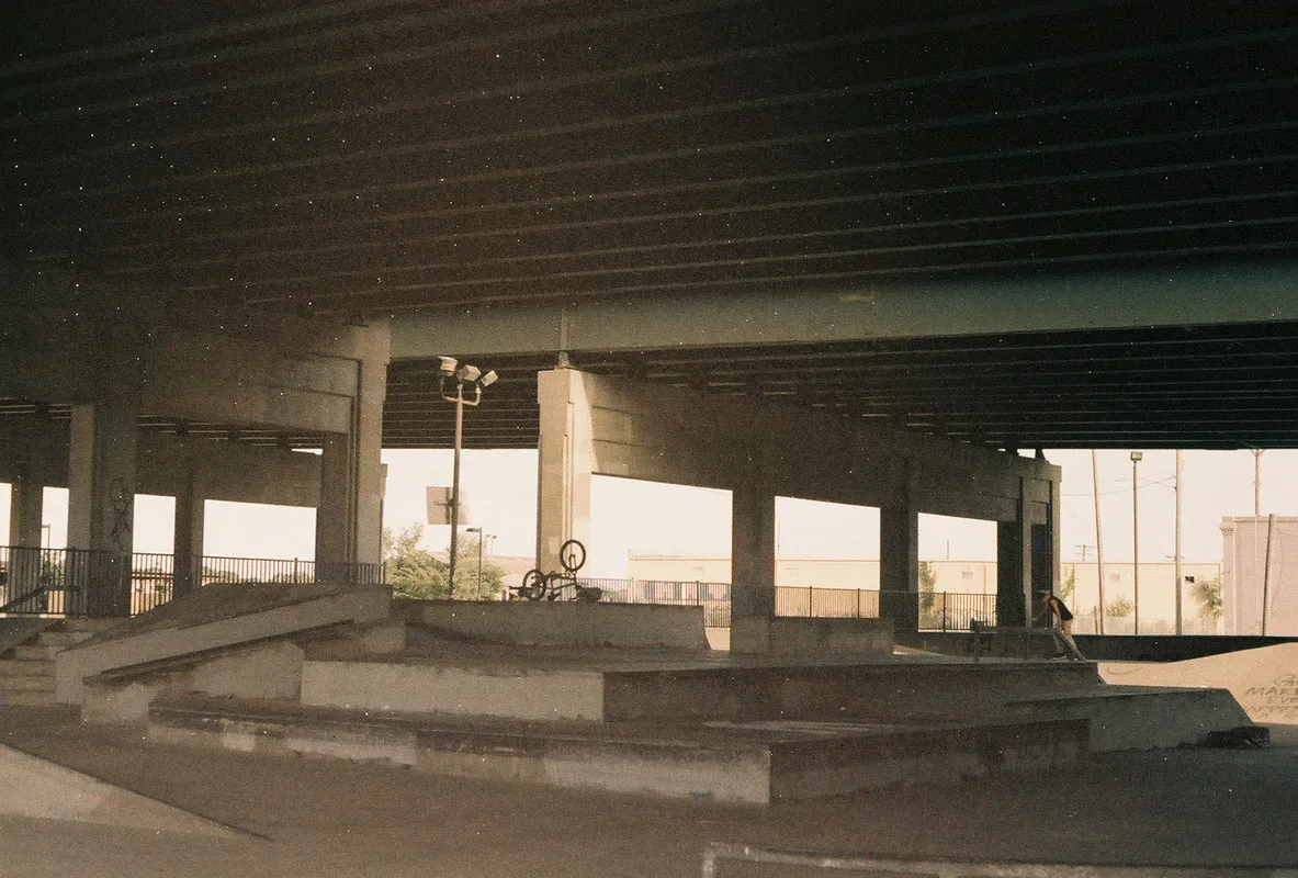 skate park underneath a highway; light coming down from between the gap between two highway overpasses illuminates a bicycle.