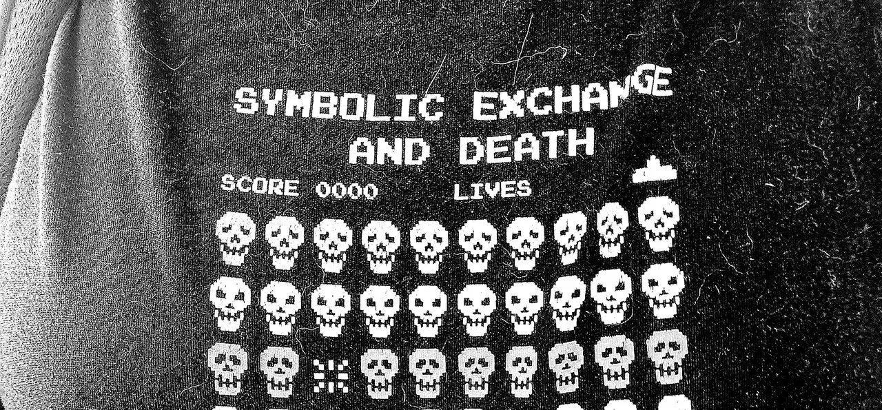 a t-shirt with _invaders_-style screenshot but the aliens are skulls. the text reads: "SYMBOLIC EXCHANGE AND DEATH; BY JEAN BAUDRILLARD"