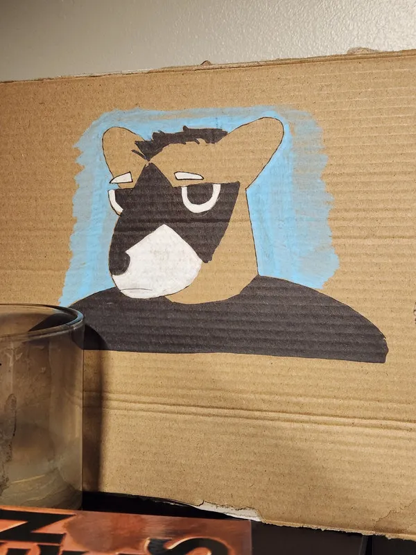 A photograph of a piece of gardboard with an anthro raccoon man illustrated on it