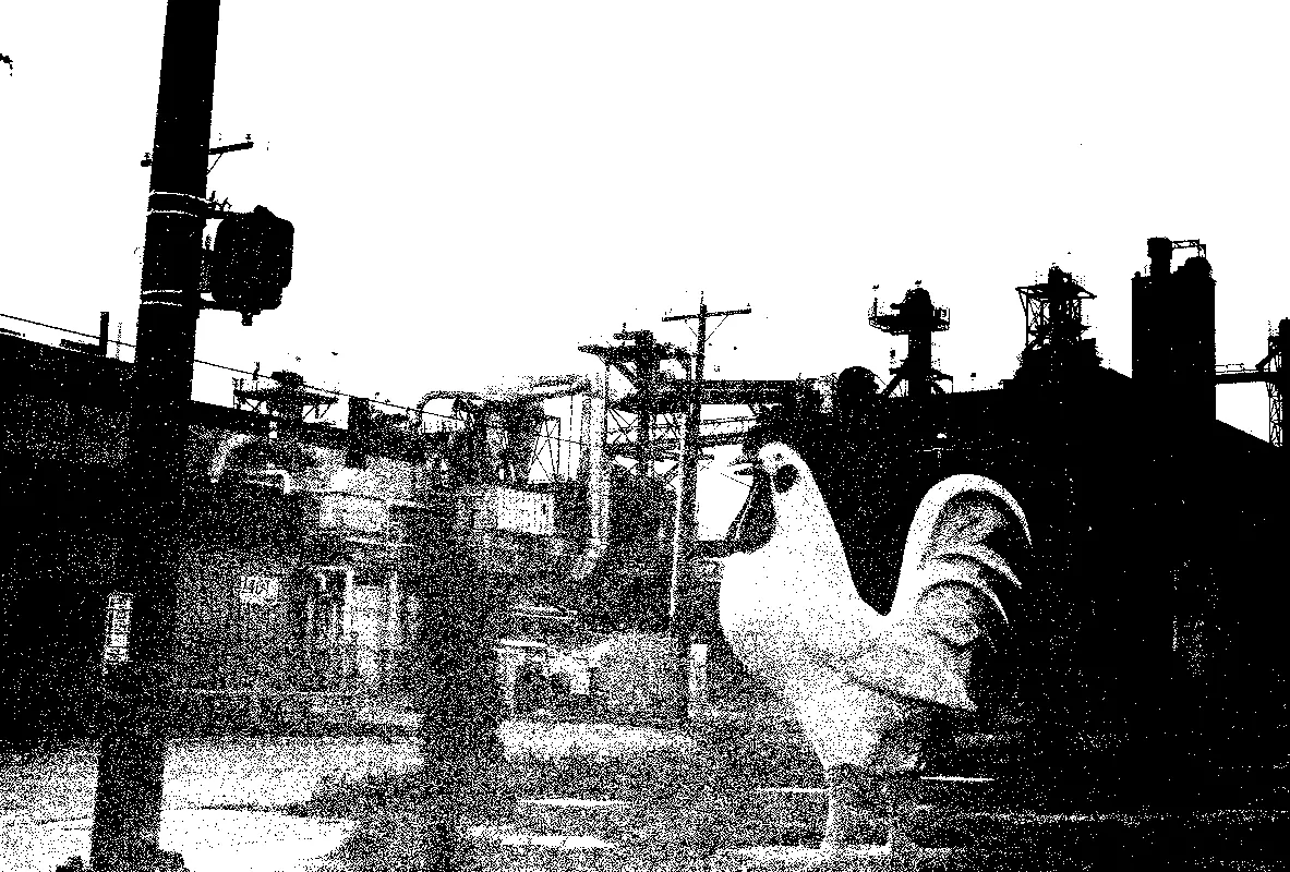 a chicken statue in front of an industrial landscape