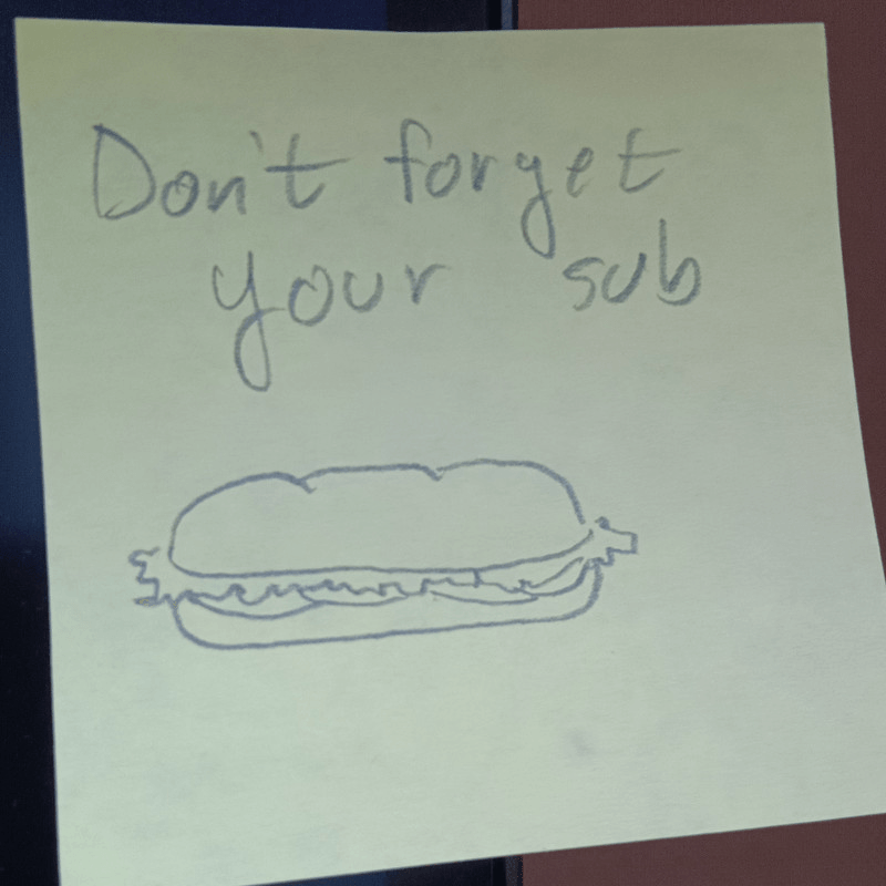 A post it note reading "Don't forget your sub" with a sketch of a sub sandwich.