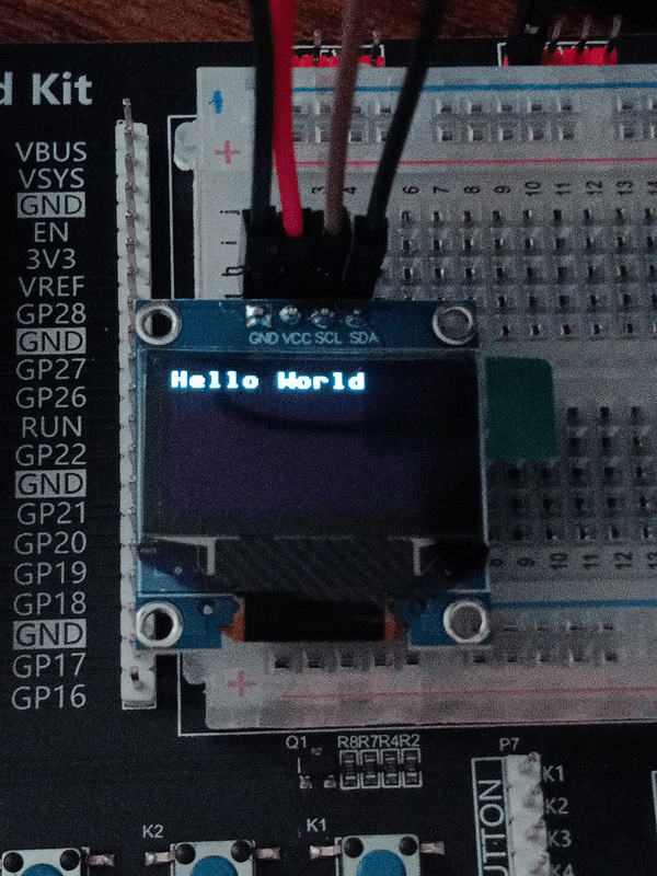 An OLED display module on a breadboard displaying the text "Hello World"