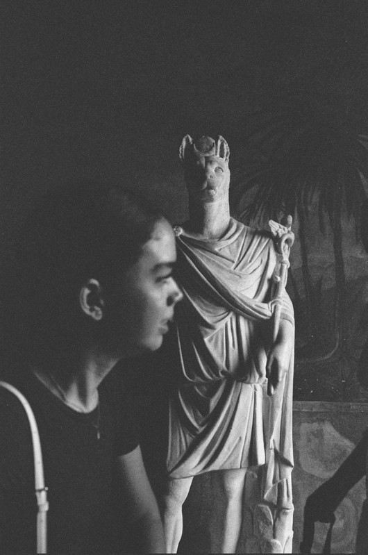 A statue of Hermanubis partially concealed by a museumgoer.